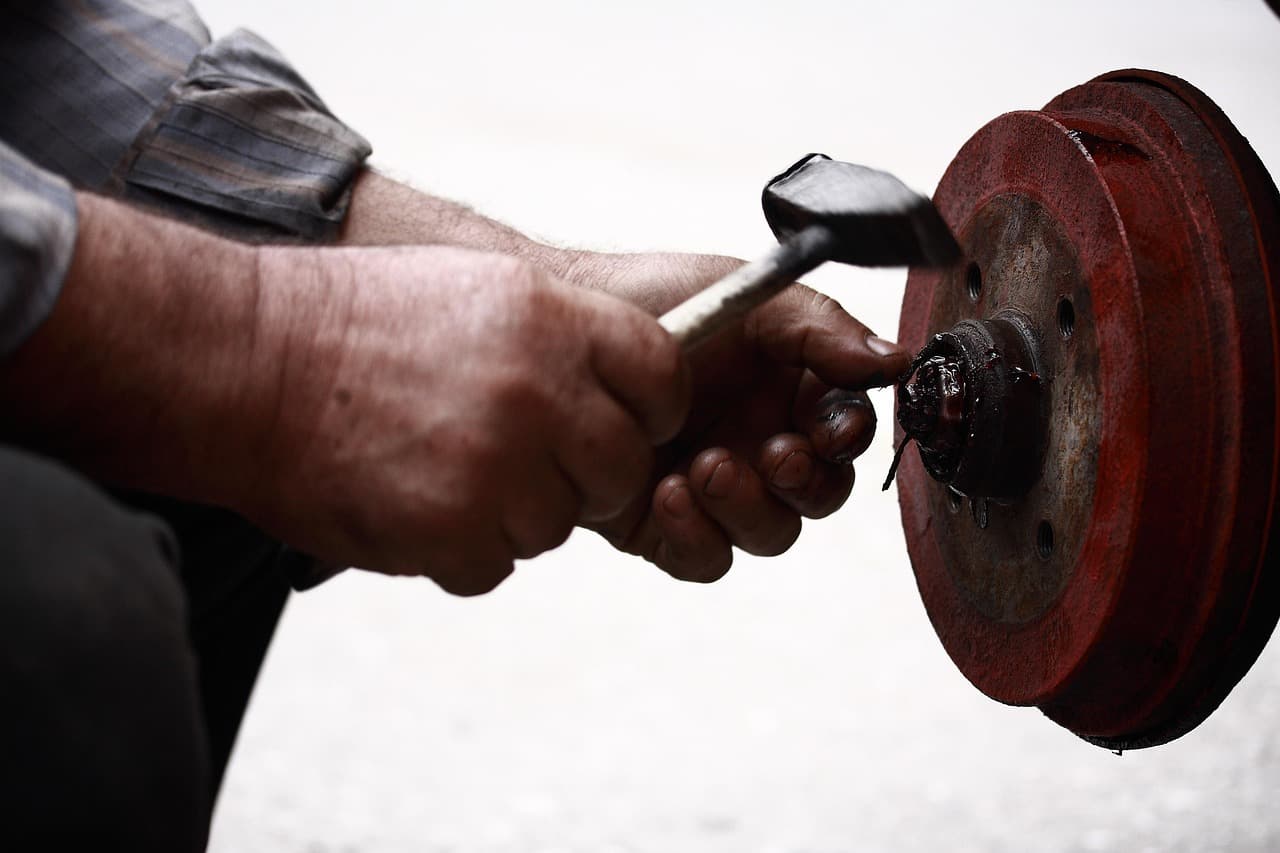 A mechanic’s hands knocking a brake drum free with a hammer