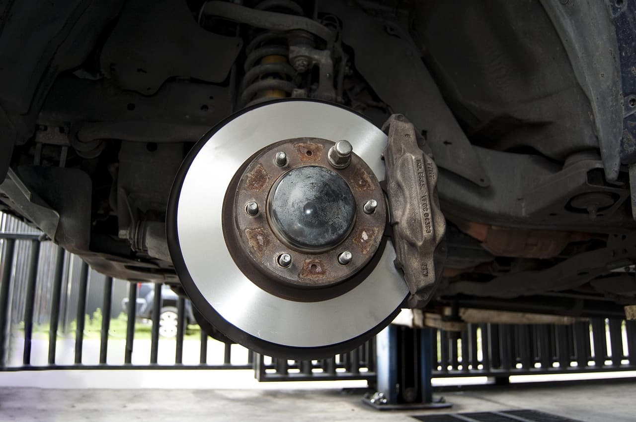 A brake disc and calliper on a car raised on a lift, wheel off