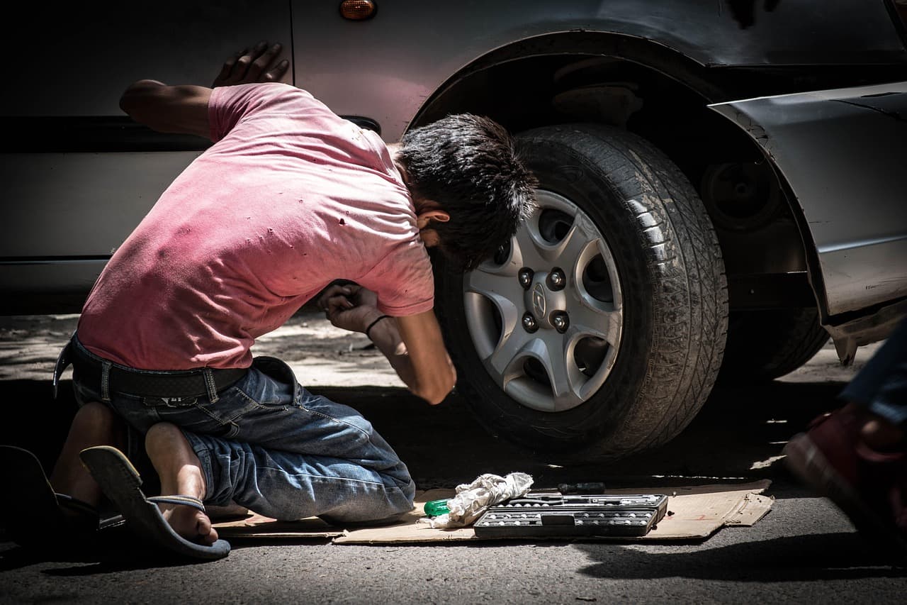 A mechanic kneeling at a car’s front wheel with his tools laid out